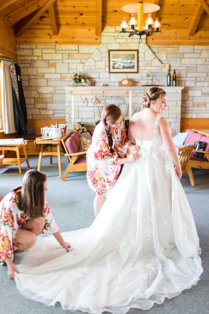 bridesmaids in floral robes buttoning bride's gown at elegant wedding at Red Crown Lodge