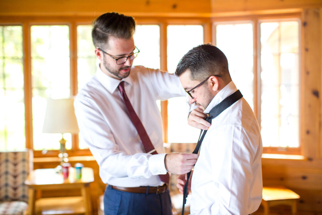 Groom helping best man with his tie at elegant wedding at Red Crown Lodge