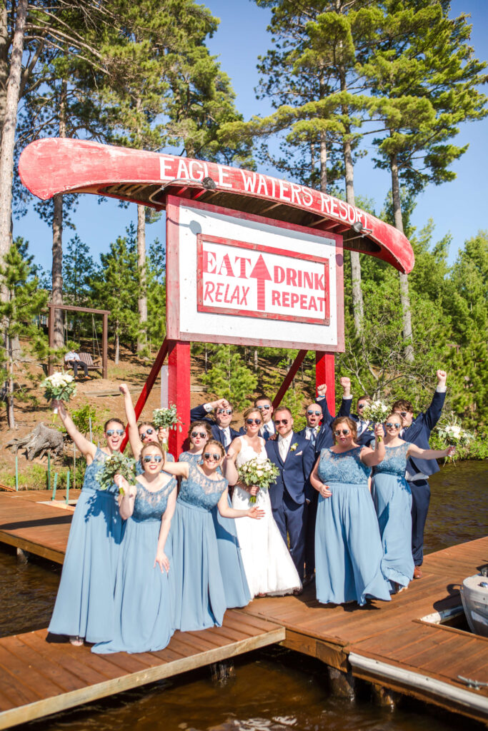 Wedding party on the main dock under the historic eagle waters canoe sign, all wearing sunglasses.