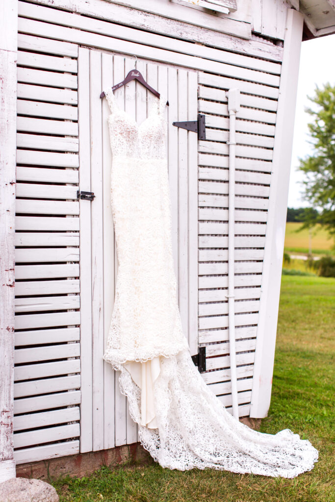 Bridal gown hanging on white barn door at summer wedding at farmin' betty's 