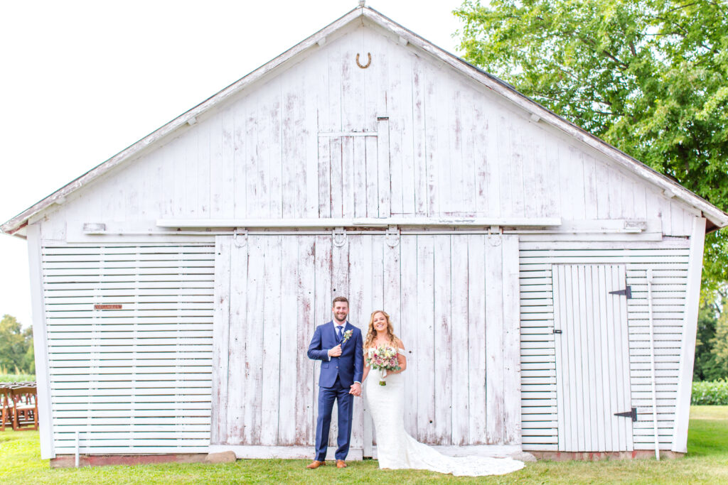 Bride & Groom posed by white barn door at summer wedding at farmin' betty's 